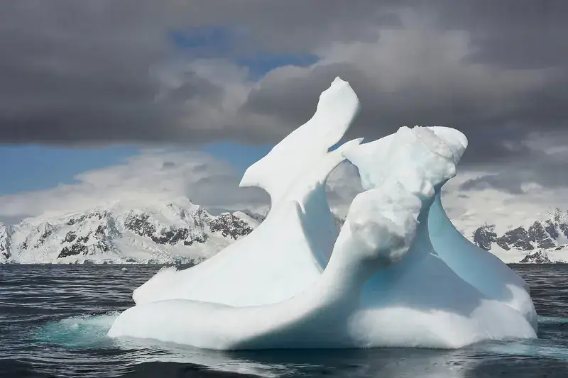 A sculpted iceberg in front of snow-covered Antarctic mountains