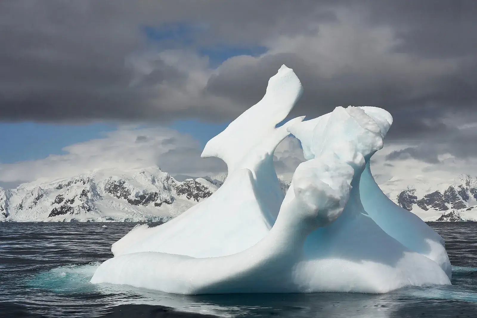 A sculpted iceberg in front of snow-covered Antarctic mountains